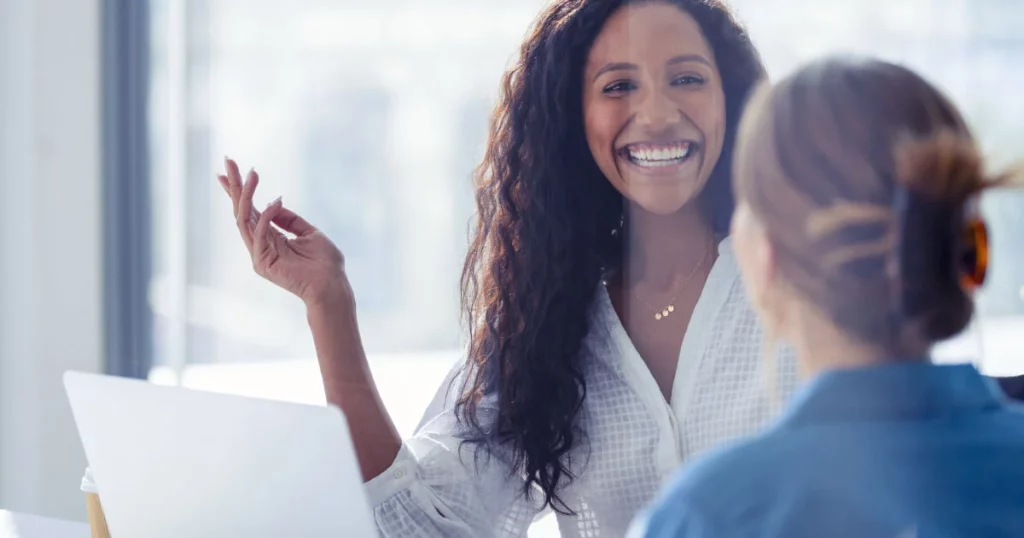 two women smiling and talking at a computer