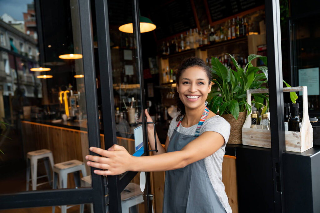 smiling woman opens door to her bar