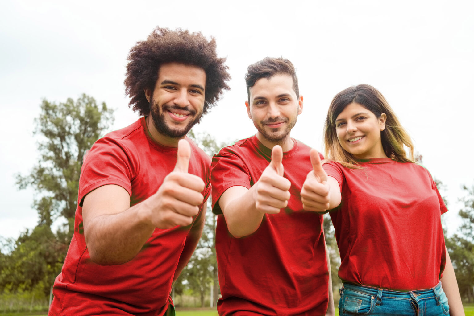three people hold up thumbs while wearing red