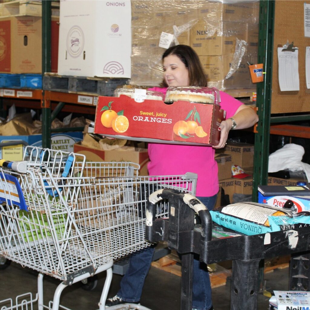 volunteer loads oranges and cakes into a shopping cart in a warehouse