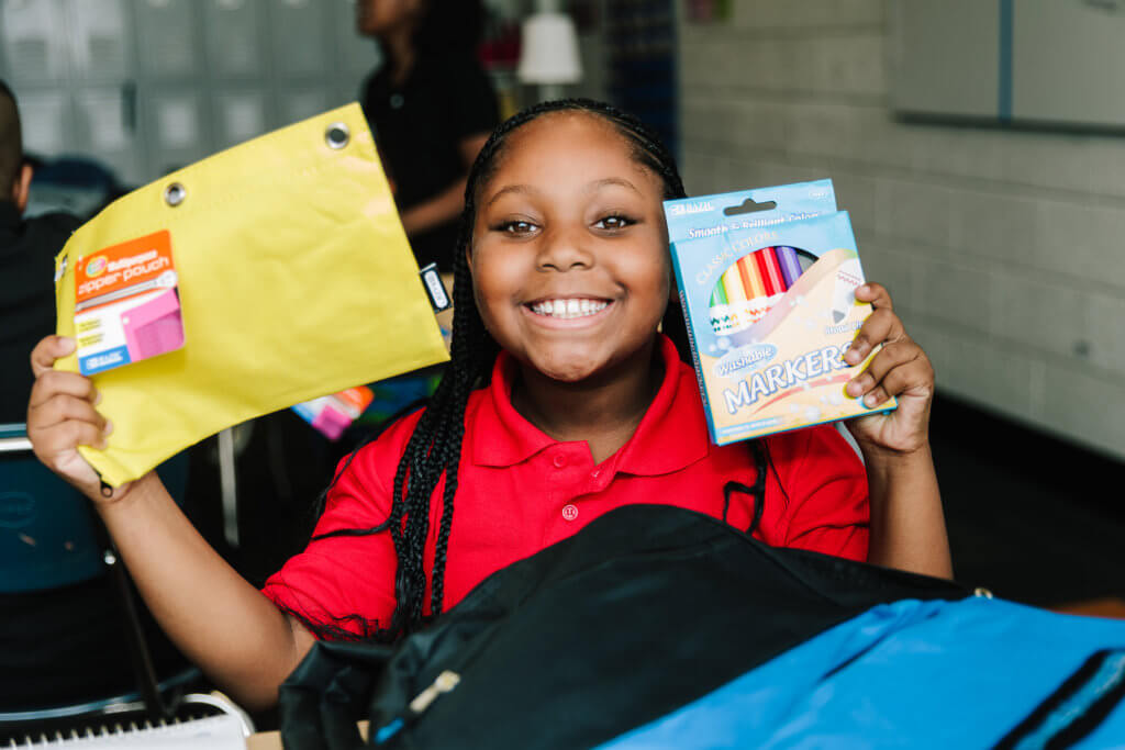 Young student holding school supplies donated by Christian Community Action