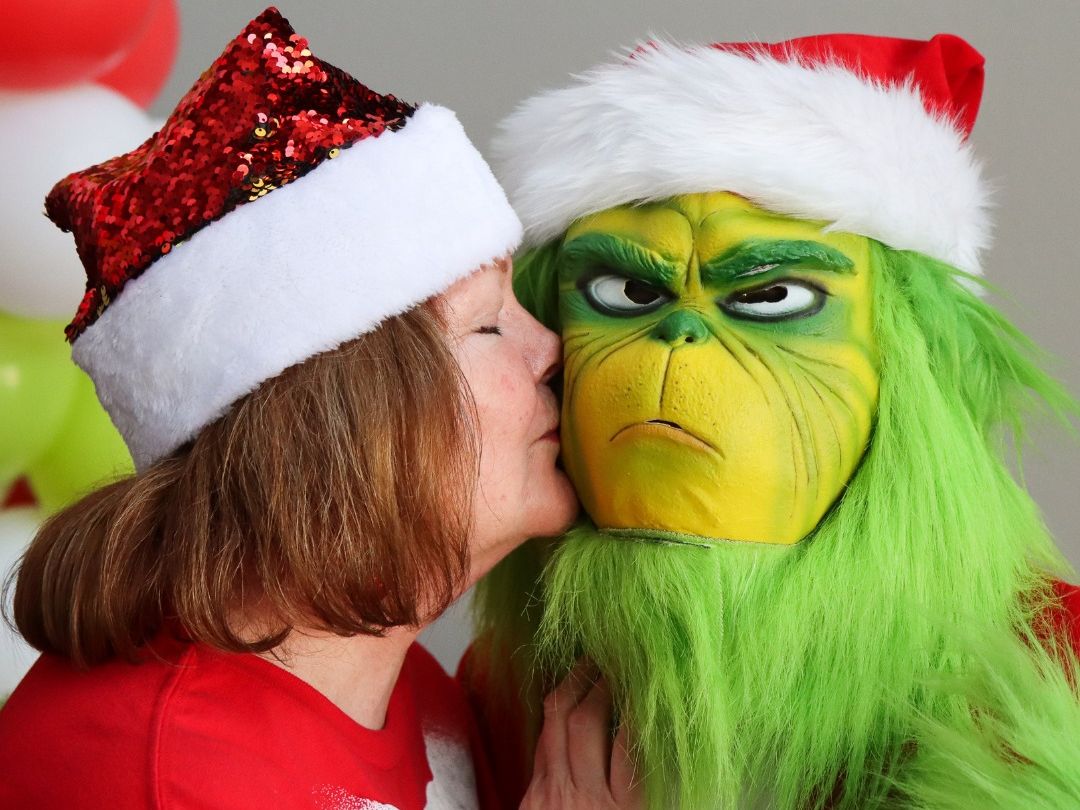 Woman kissing the Grinch on the cheek to spread Christmas cheer.