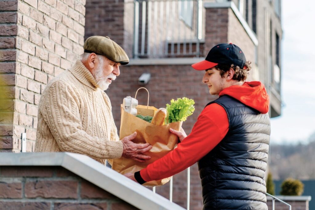 Young man volunteering by delivering groceries to senior citizen.