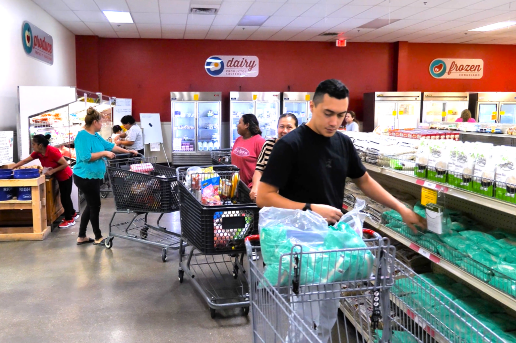 Volunteer stocking shelves in the food pantry with shoppers pushing carts nearby